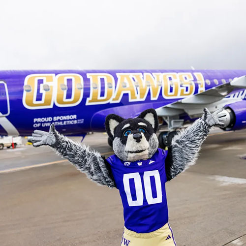 UW Husky mascot in front of airplane that says 'Go Dawgs'